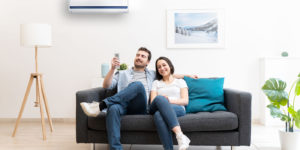 a couple sitting on the couch while adjusting their ductless ac system
